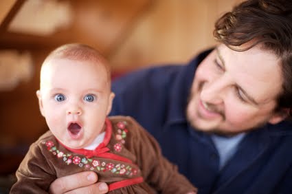 Dad with brown hair holds baby making surprised face